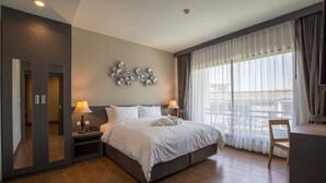 A modern hotel room with a large bed, bedside lamps, a desk, and a view of the city through large windows. - Civilize Hotel (Udon Thani)