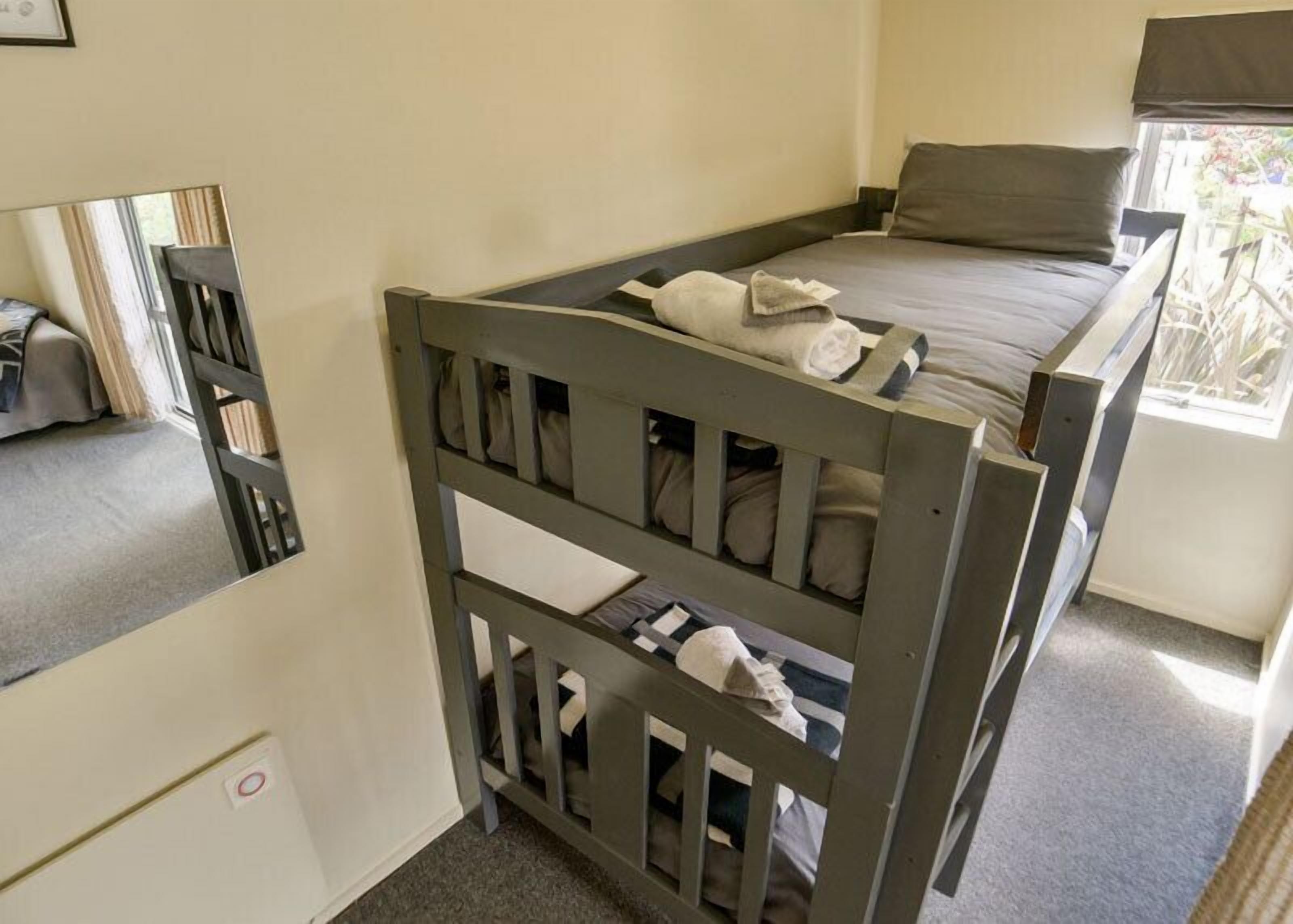 A single bed with a headboard, a window with curtains, and a mirror on the wall.