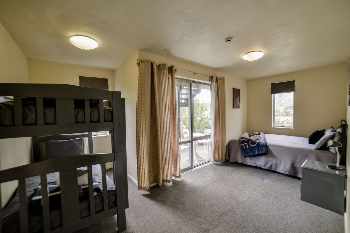 A bedroom with a bunk bed, a single bed, a desk, and a window.
