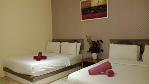 Habitación de hotel con dos camas, cada una con sábanas blancas y toallas rosas. Entre las camas, hay una mesita con un jarrón de flores.
