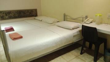 A single bed with white bedding, a desk with a telephone, and a chair.