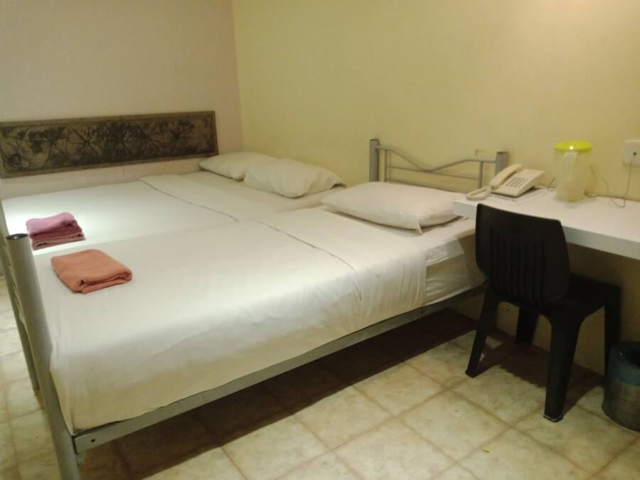 A single bed with white bedding, a desk with a telephone, and a chair.