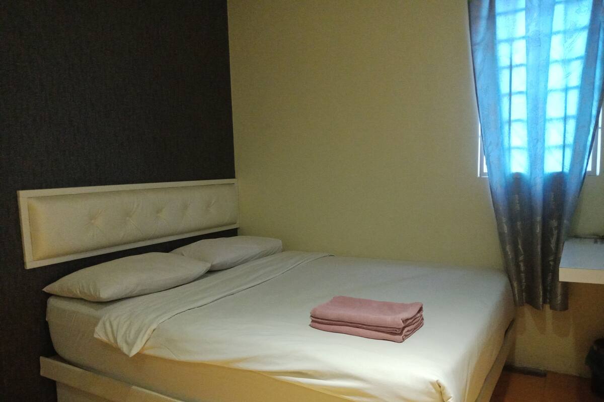 A single bed with a headboard, a bedside table, and a window with curtains.
