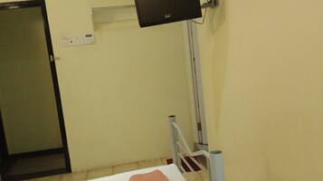 A room with two beds, a flat-screen TV mounted on the wall, an air conditioning unit, and a door.