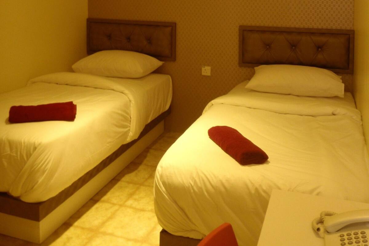 A hotel room with two beds, a telephone, and a wall-mounted light fixture.