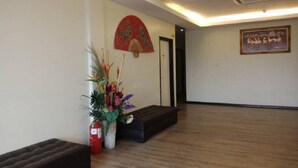 Un lobby espacioso con piso de madera, un sofá negro, un arreglo de plantas decorativo, un ventilador rojo y un letrero de bienvenida enmarcado.