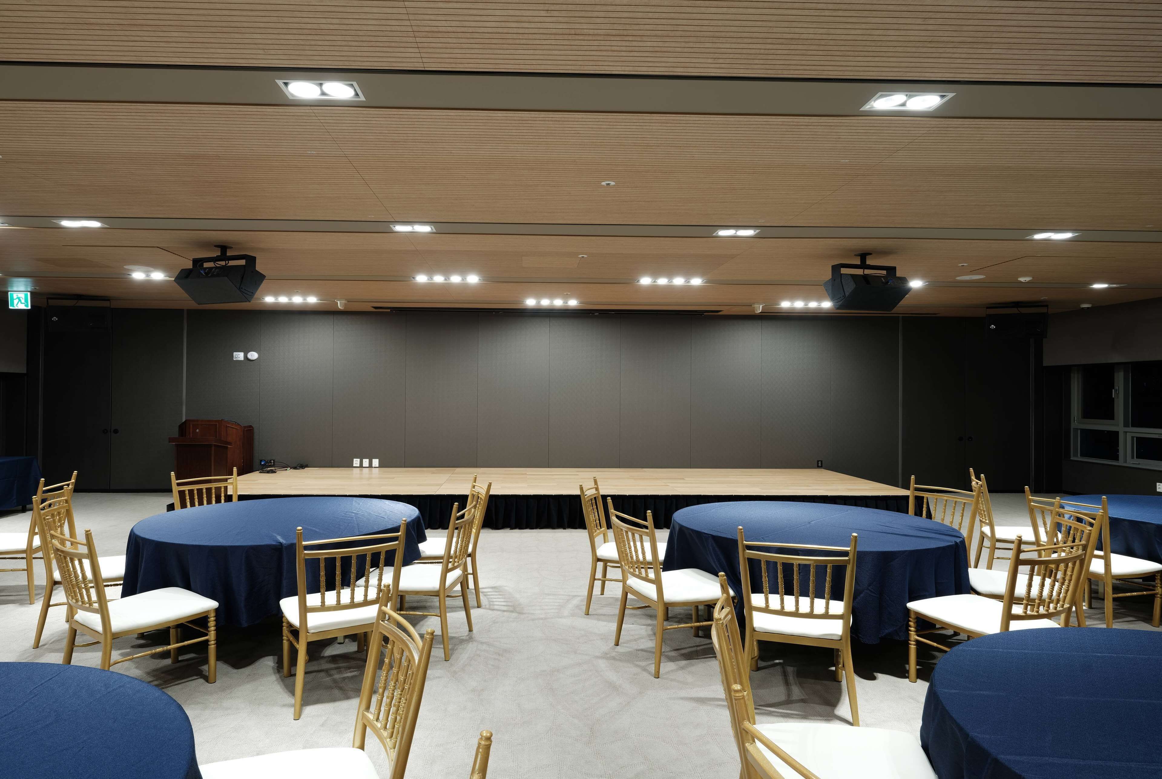 Un salón de conferencias con una mesa larga, mesas redondas y sillas de madera.