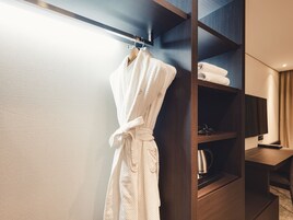 Habitación de hotel con un armario de madera, una bata colgada en la puerta y un televisor de pantalla plana sobre una mesa de madera.