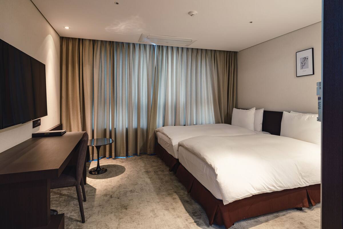 A hotel room with a bed, a desk, a chair, a TV, and a window with curtains.