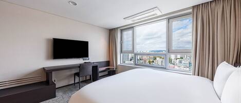 Habitación de hotel con una cama grande, un escritorio con silla, televisor de pantalla plana montado en la pared y un ventanal con vistas a la ciudad.
