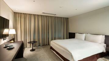A hotel room with a bed, a desk with a lamp, a flat-screen TV, and a large window with curtains.