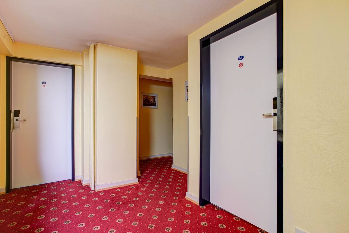A hallway with patterned carpet, doors with room numbers, and a partial view of a room with a bed.