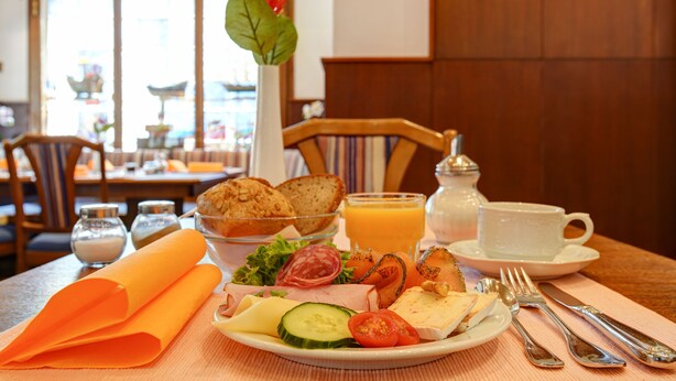 A breakfast setting with a plate of food, a glass of orange juice, and a vase with a flower. - Hotel Elbinsel (Hamburg)