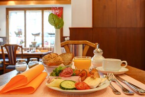 A breakfast setting with a plate of food, a glass of orange juice, and a vase with a flower.