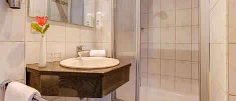 A bathroom with a sink, mirror, and shower.