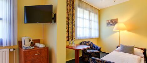 A hotel room with a bed, a desk, a chair, a television, and a window with curtains.