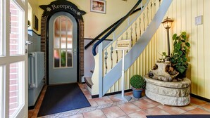 A reception area with a staircase, a reception sign, a potted plant, and a radiator. - Hotel Elbinsel (Hamburg)