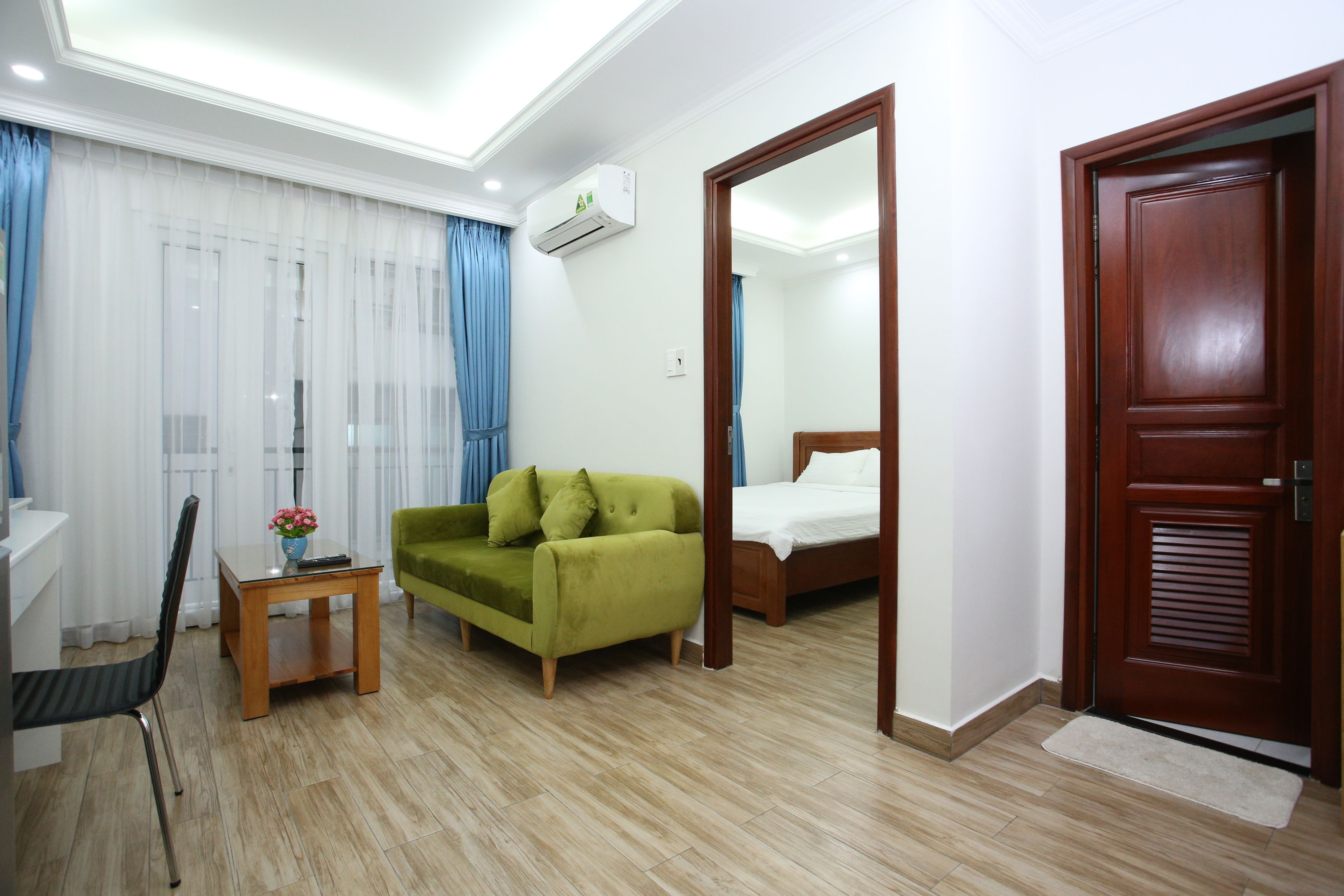 Ein Hotelzimmer mit Holzboden, einem grünen Sofa, einem hölzernen Bett, einem kleinen Tisch mit einer Vase und einem Spiegel an der Wand.