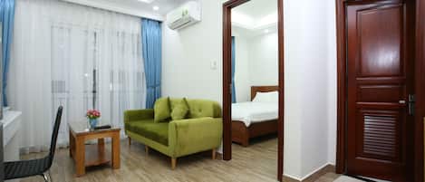A hotel room with a wooden floor, a green sofa, a wooden bed, a small table with a vase, and a mirror on the wall.