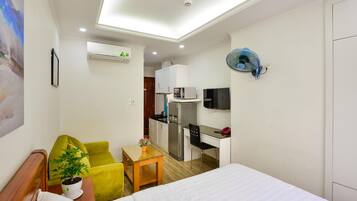 Habitación de hotel con cama, escritorio, silla, una pequeña mesa con planta y una kitchenette.