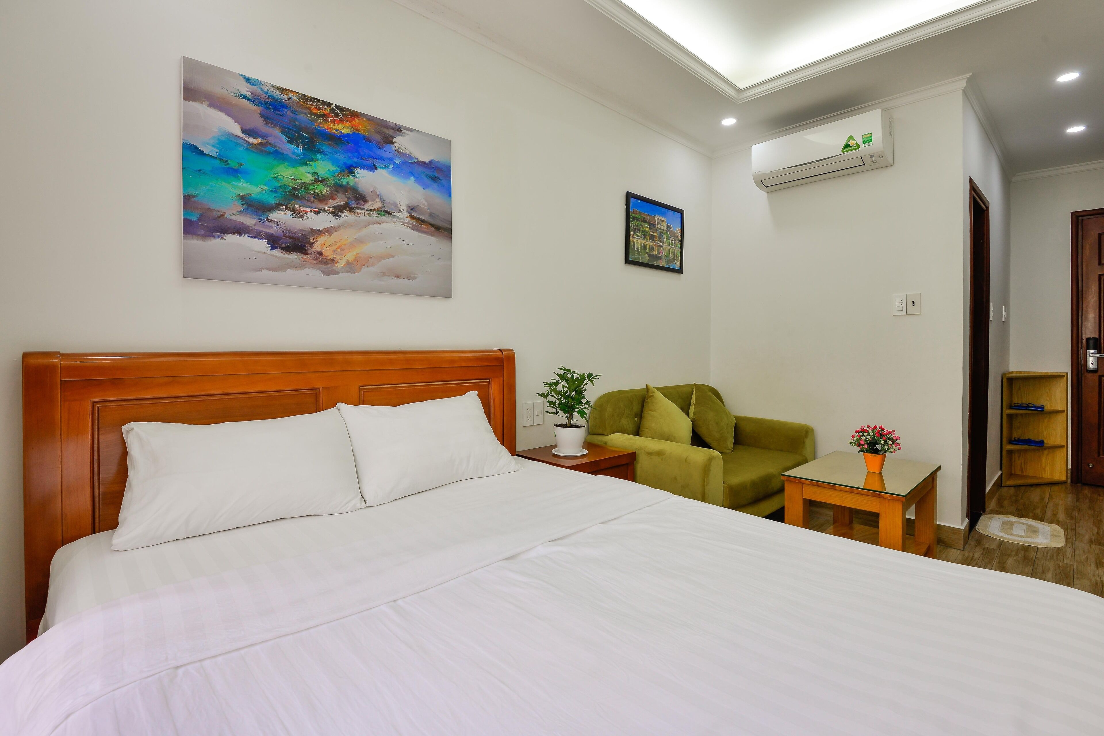 Ein Hotelzimmer mit einem großen Bett, einem grünen Sessel, einem kleinen Tisch mit einer Vase und einem Gemälde an der Wand.