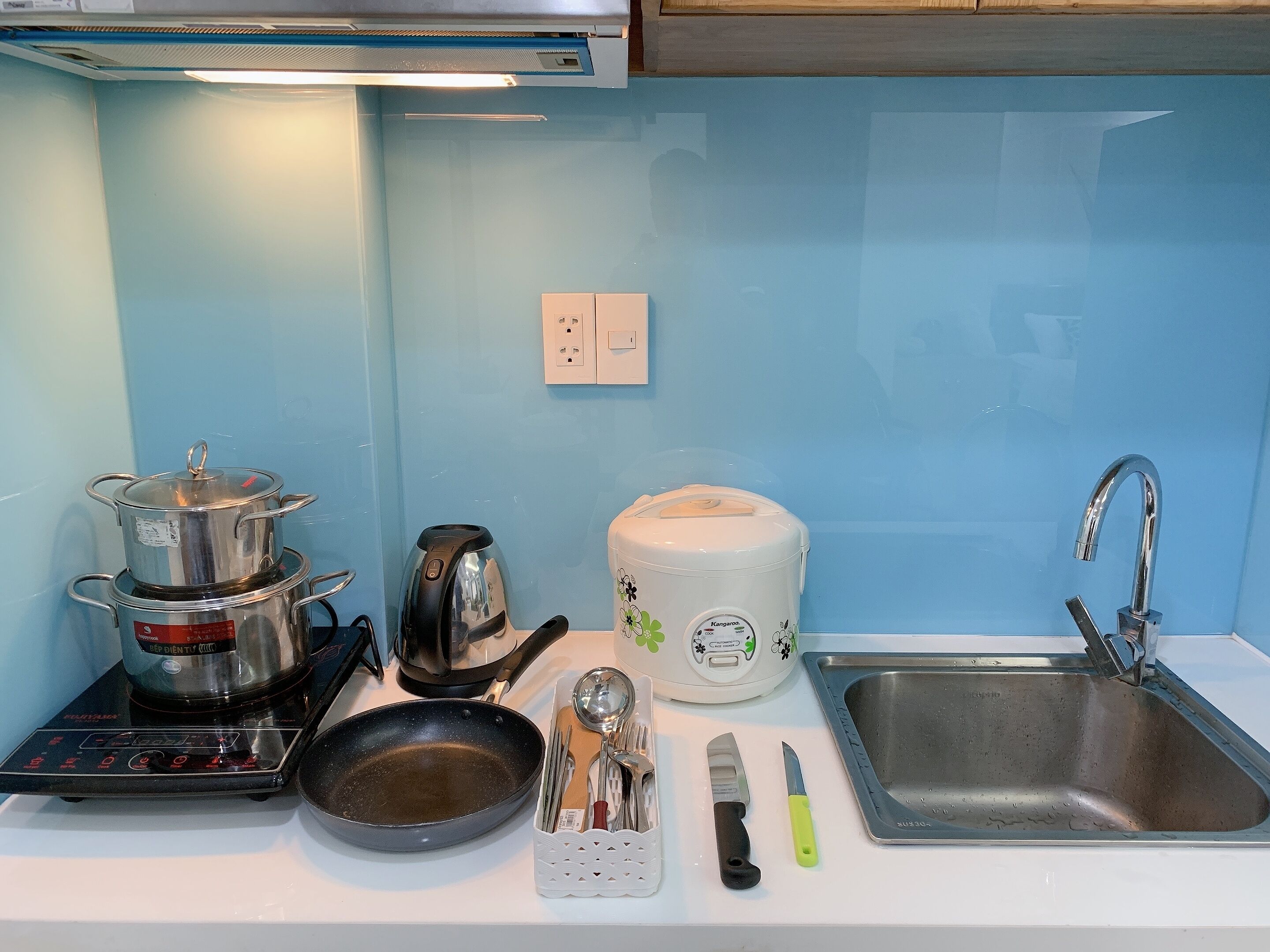 A kitchen with a stove, kettle, toaster, sink, and utensils.