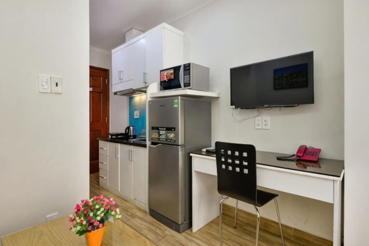 A compact kitchen with a refrigerator, microwave, and a flat-screen TV.