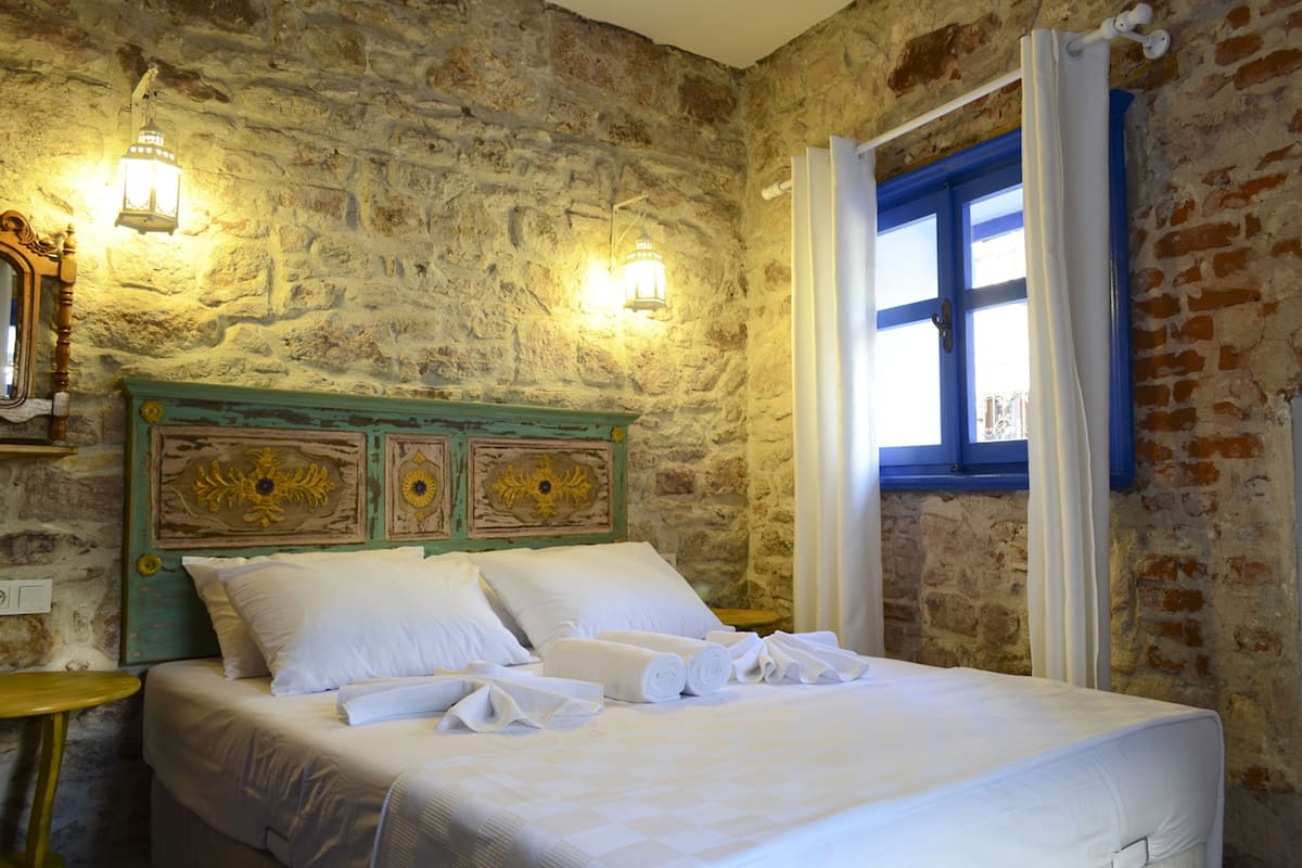 A bed with white linens and towels, a stone wall, and two wall-mounted lights.