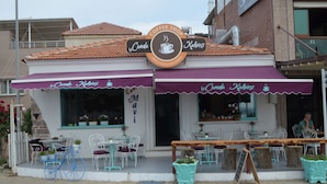 A coffee shop with outdoor seating, a signboard, and a wooden bench. - Cunda Mavi Otel - Adults Only (Ayvalik)