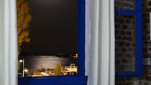 A view from a window with a blue frame, overlooking a body of water with a boat and some buildings in the distance. - Cunda Mavi Otel - Adults Only (Ayvalik)