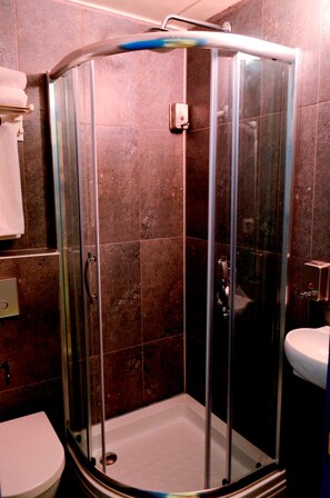 Eine Duschkabine mit Glasfront, ein weißes Waschbecken und eine Toilette zur Linke.