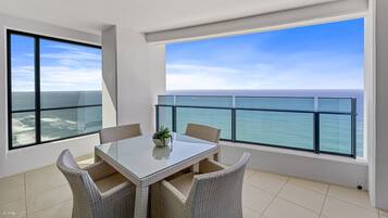 Un balcon doté d’une balustrade en verre, une table à manger avec des chaises et une vue sur l’océan.