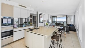 A modern kitchen with a central island, stainless steel appliances, and a dining area with a view. - Esplanade (Soul) - Apartment Stay Private (Surfers Paradise)