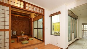 A traditional Japanese-style room with tatami flooring, a low wooden table, cushions, and a sliding glass door leading to a balcony. - Flowerinn (Magong)