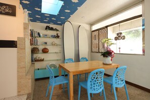 A dining area with a wooden table, blue chairs, a bookshelf, and surfboards against the wall. - Flowerinn (Magong)