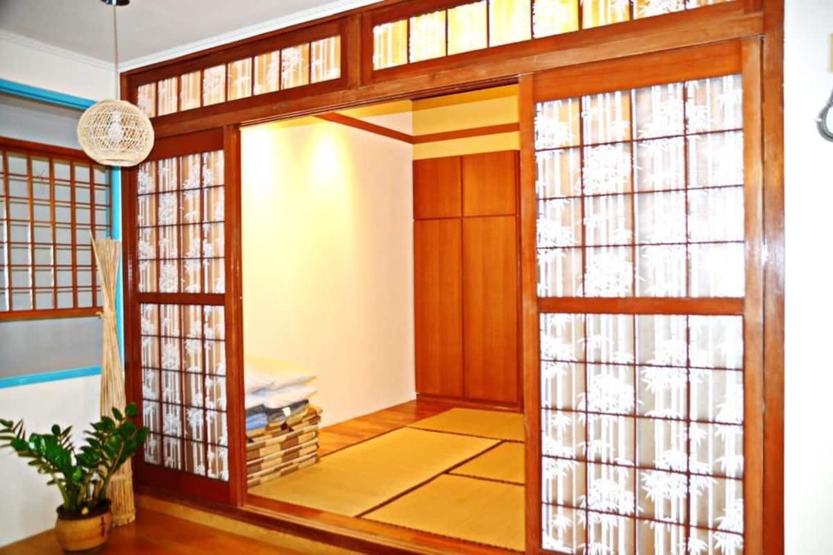 A traditional Japanese room with tatami flooring, sliding doors, and a small table with books and a plant.
