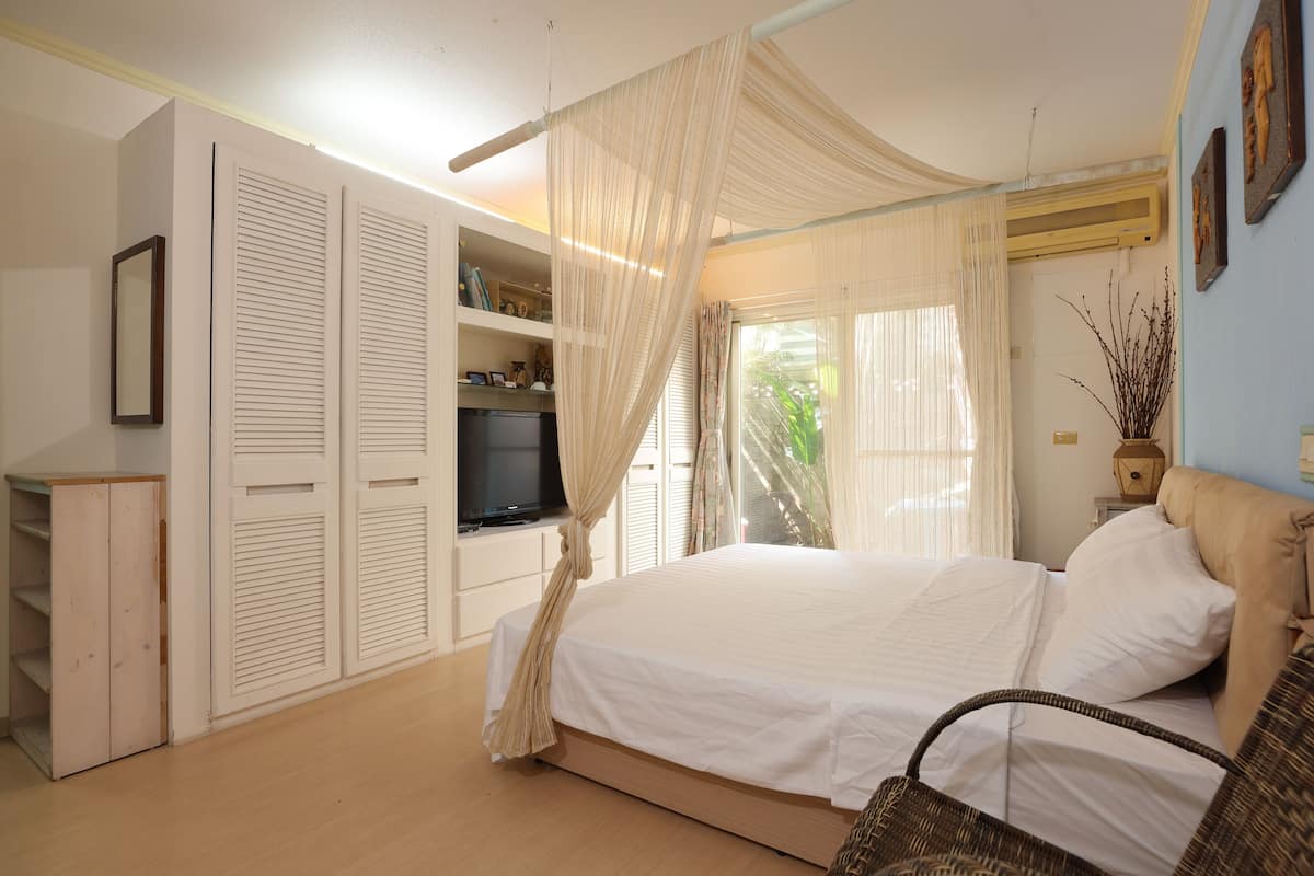 A bedroom with a bed, a television, a wardrobe, and a window with curtains.