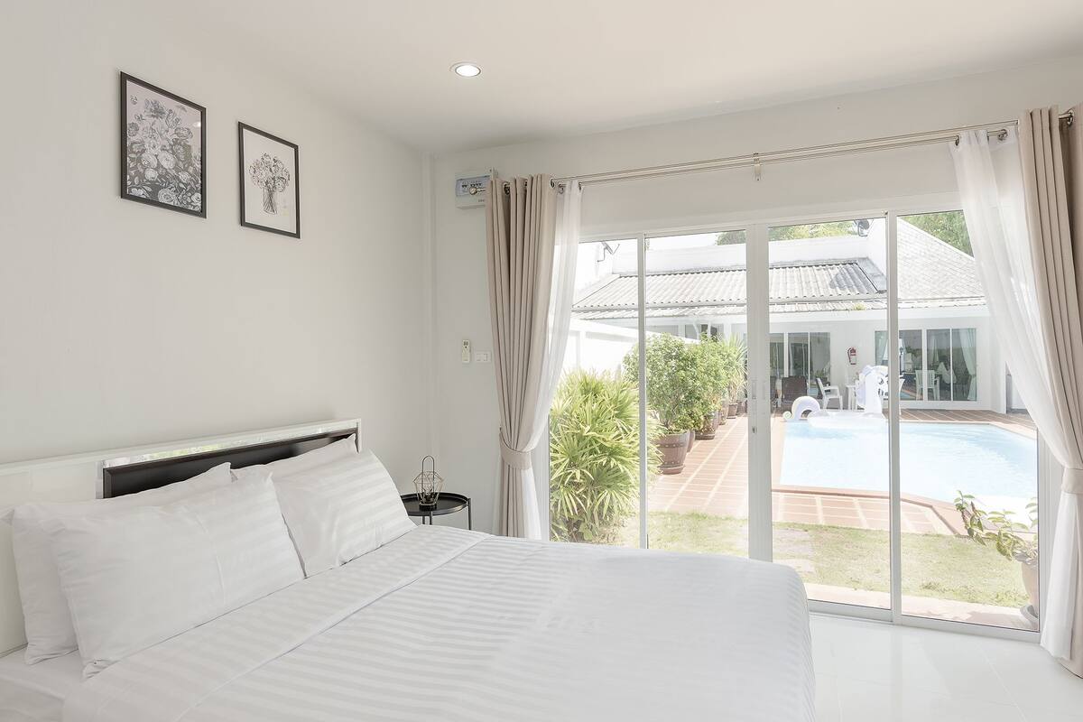 Une chambre dotée d’un grand lit, d’une table de chevet et offrant une vue sur une piscine et un espace extérieur.