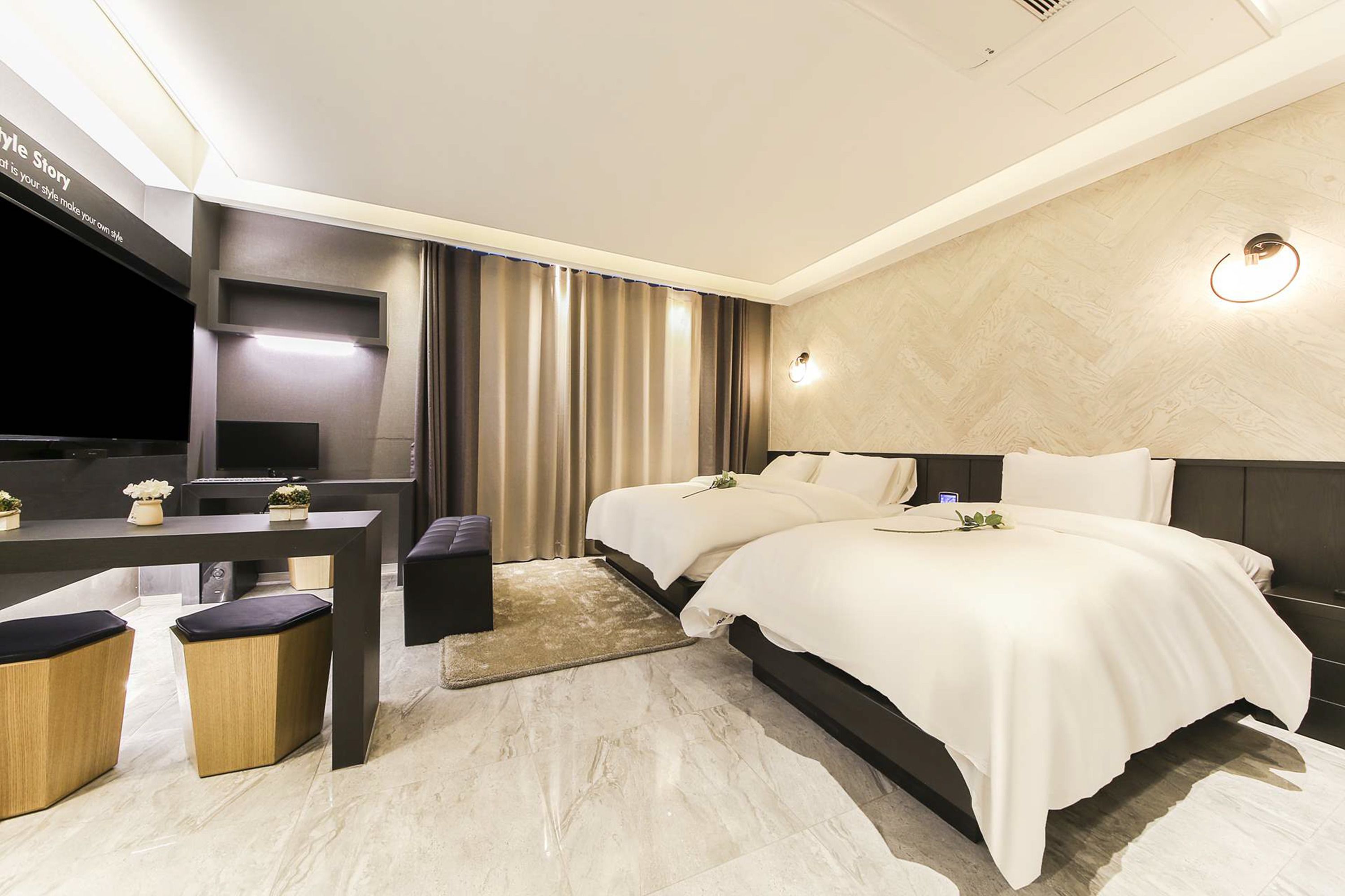 Una habitación de hotel moderna con una cama grande, un escritorio con televisión de pantalla plana y una zona de estar con otomanas.
