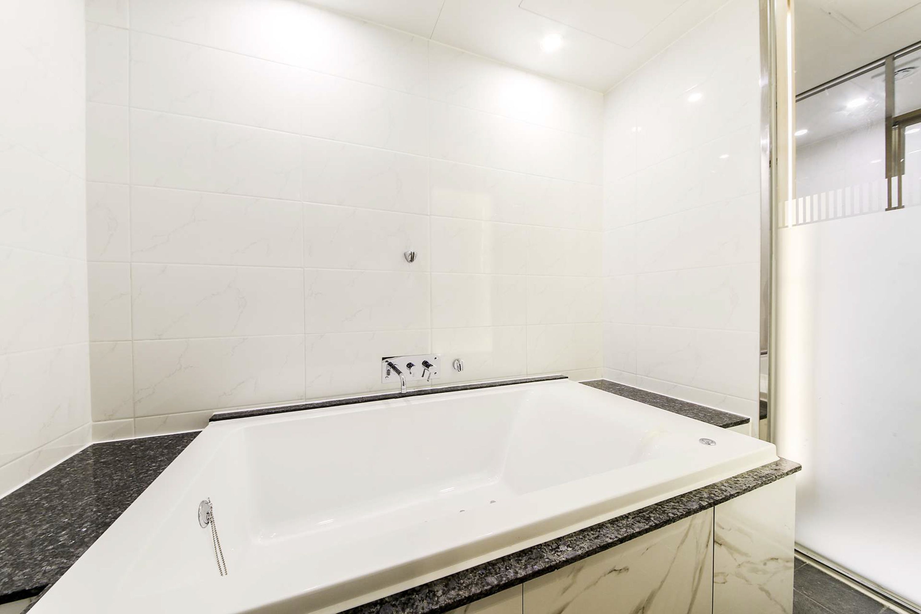 Un baño moderno con una bañera grande, encimeras de mármol y paredes cubiertas de azulejos blancos.