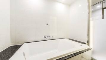 Un baño moderno con una bañera grande, encimeras de mármol y paredes cubiertas de azulejos blancos.