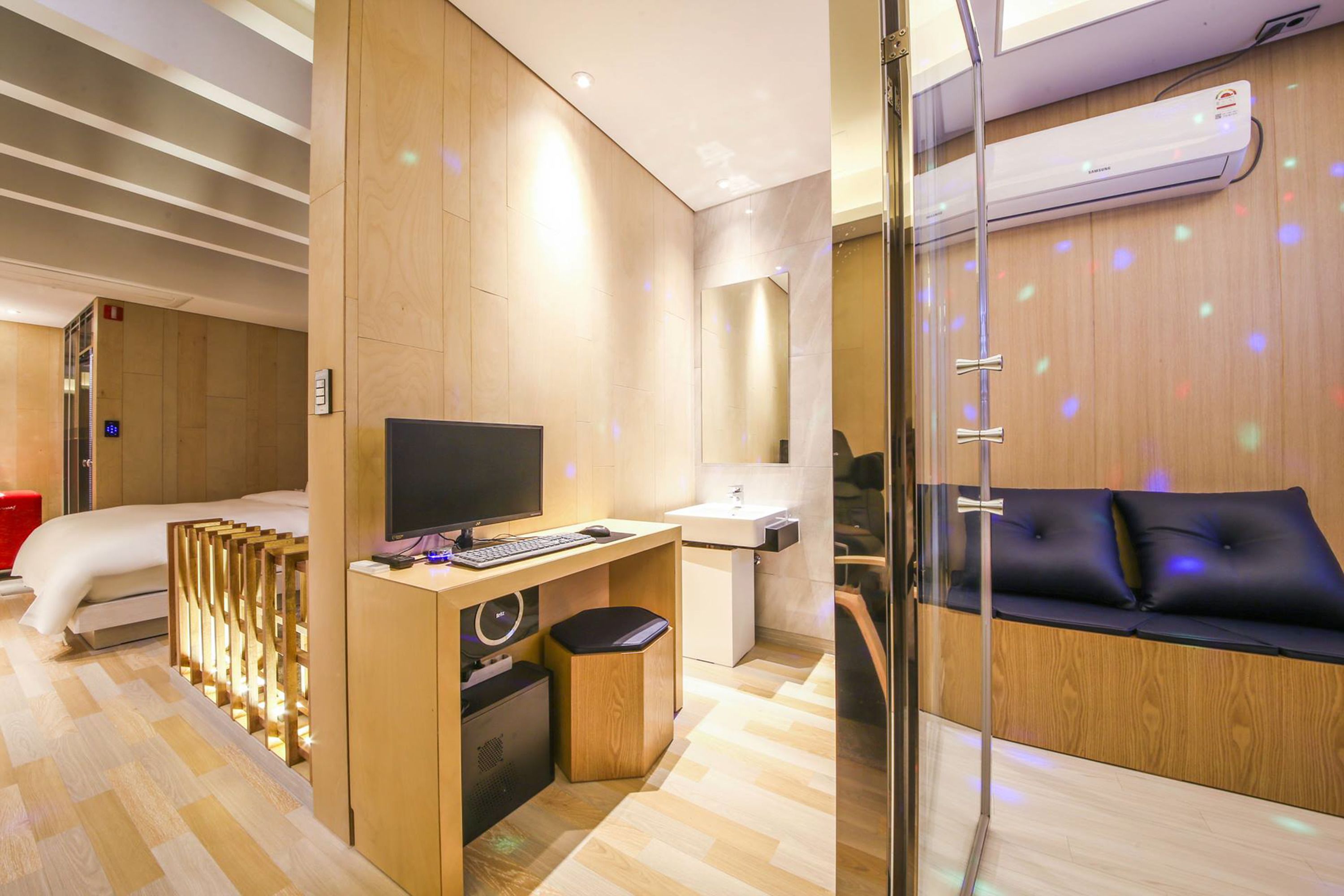 A modern hotel room with a wooden desk, a bed, a sofa, and a glass partition.