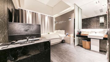A modern hotel room with a large bed, a bedside table with a lamp, a vanity with a mirror, and a black marble desk.