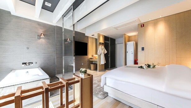 A modern hotel room with a large bed, a separate bathroom with a bathtub, a small sitting area, and a shower area. - HOTEL OSCAR (Daegu)