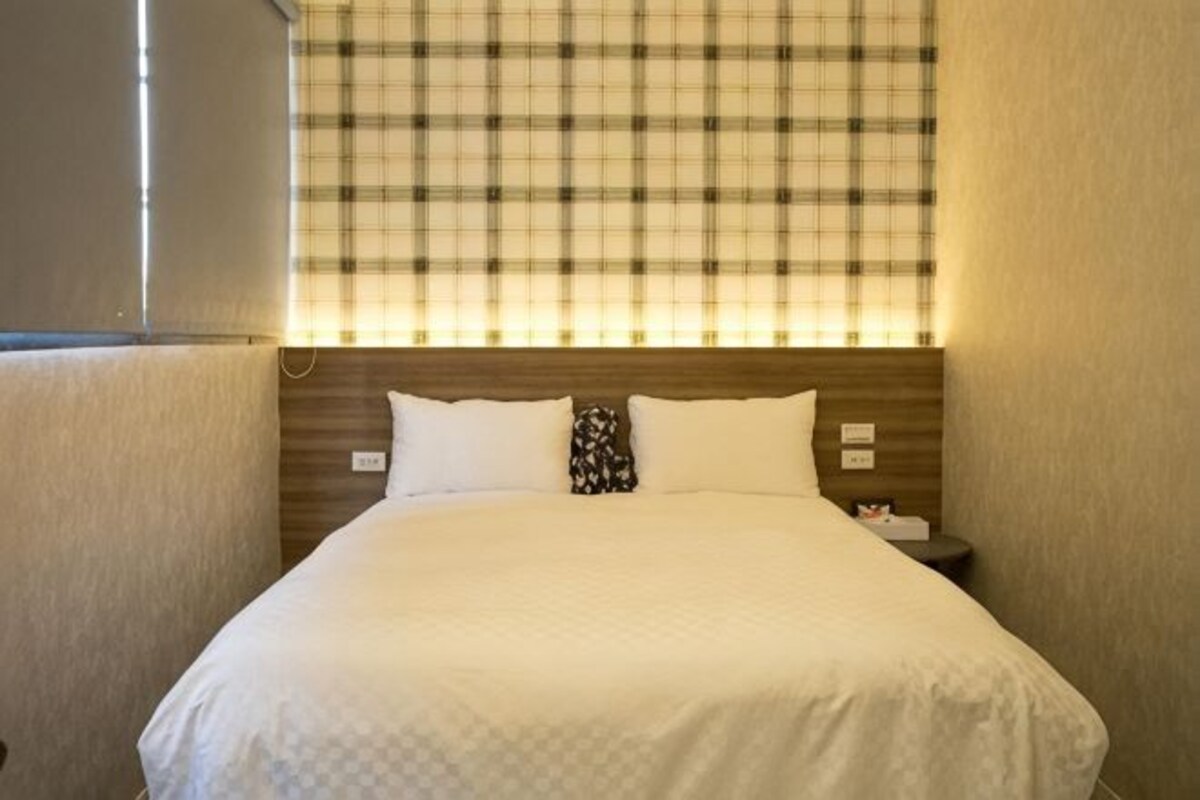 Habitación de hotel con una cama grande, cabecera con estampado escocés y mesita de noche con lámpara.