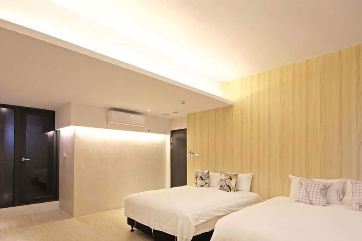 A hotel room with two beds, a wardrobe, a built-in air conditioning unit, and a wooden panel wall.