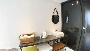 A compact kitchenette with a white sink, a coffee maker, and a basket of bread. There is a green chair and a small table with two cups. - PS Hotel (Jiaoxi)