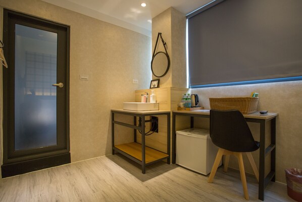 Una habitación pequeña con escritorio, silla, lavamanos y refrigerador compacto.