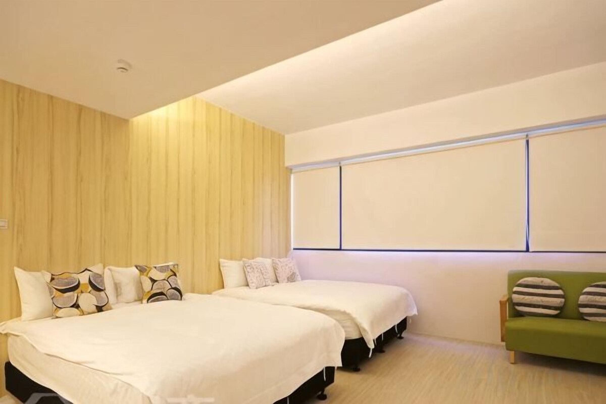 Habitación de hotel con dos camas, un sofá verde y un ventanal grande.