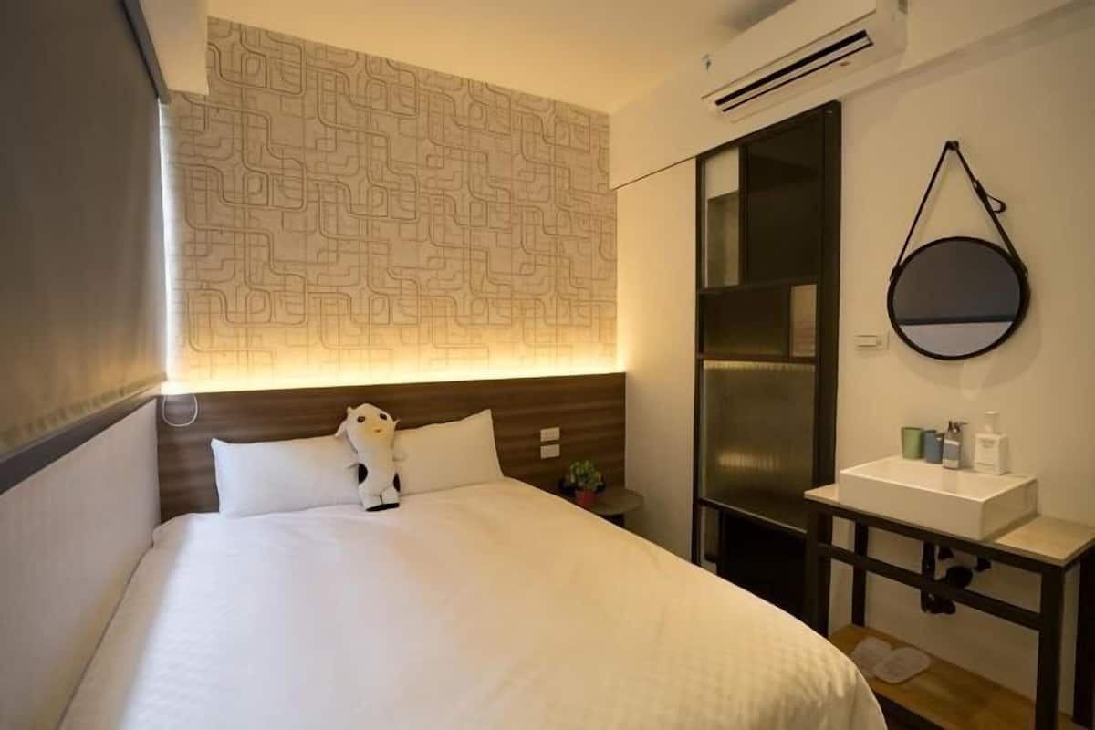 A hotel room with a bed, a nightstand, a mirror, and a wall-mounted sink.